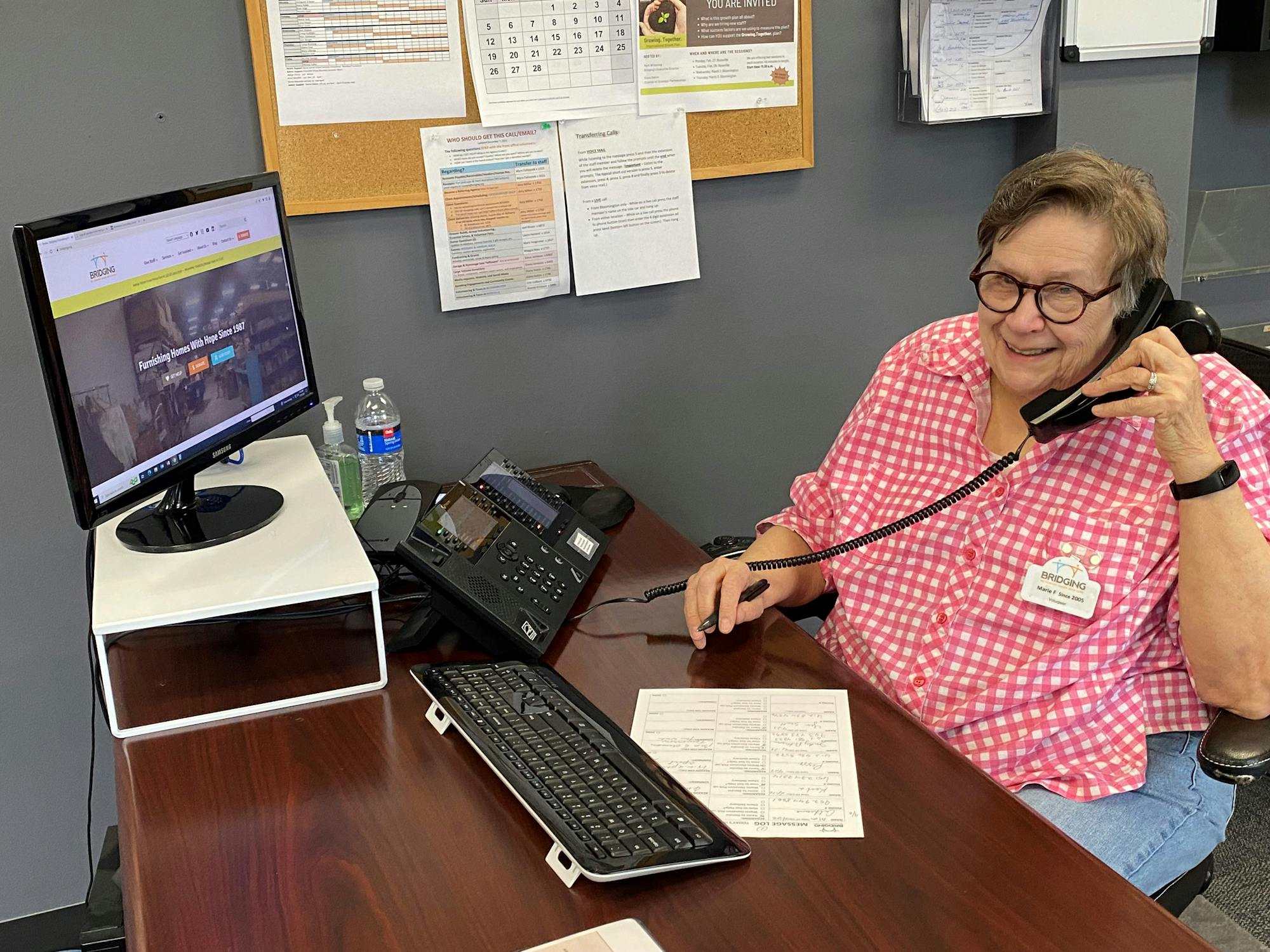 A woman sitting at a desk and wearing a nametag answers a phone.