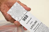 In this file photo, a bookmark for children with the 988 suicide and crisis lifeline emergency telephone number is displayed by Lance Neiberger, a volunteer with the Natrona County Suicide Prevention Task Force, while they speak about mental health and suicide awareness in Casper, Wyoming on Aug. 14, 2022. (Patrick T. Fallon/AFP via Getty Images/TNS) ORG XMIT: 86104689W