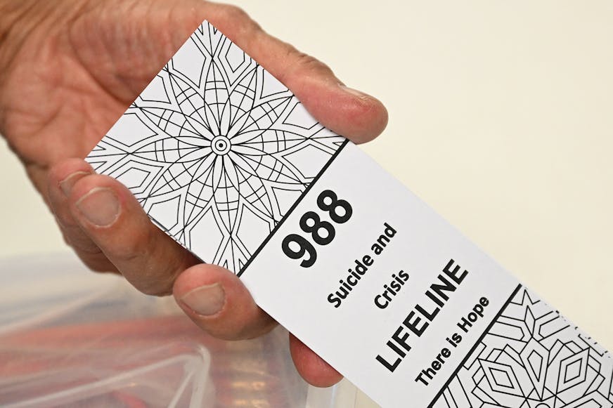 In this file photo, a bookmark for children with the 988 suicide and crisis lifeline emergency telephone number is displayed by Lance Neiberger, a volunteer with the Natrona County Suicide Prevention Task Force, while they speak about mental health and suicide awareness in Casper, Wyoming on Aug. 14, 2022. (Patrick T. Fallon/AFP via Getty Images/TNS) ORG XMIT: 86104689W