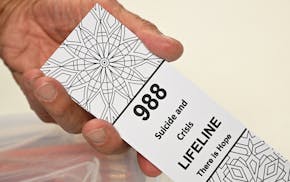 In this file photo, a bookmark for children with the 988 suicide and crisis lifeline emergency telephone number is displayed by Lance Neiberger, a vol