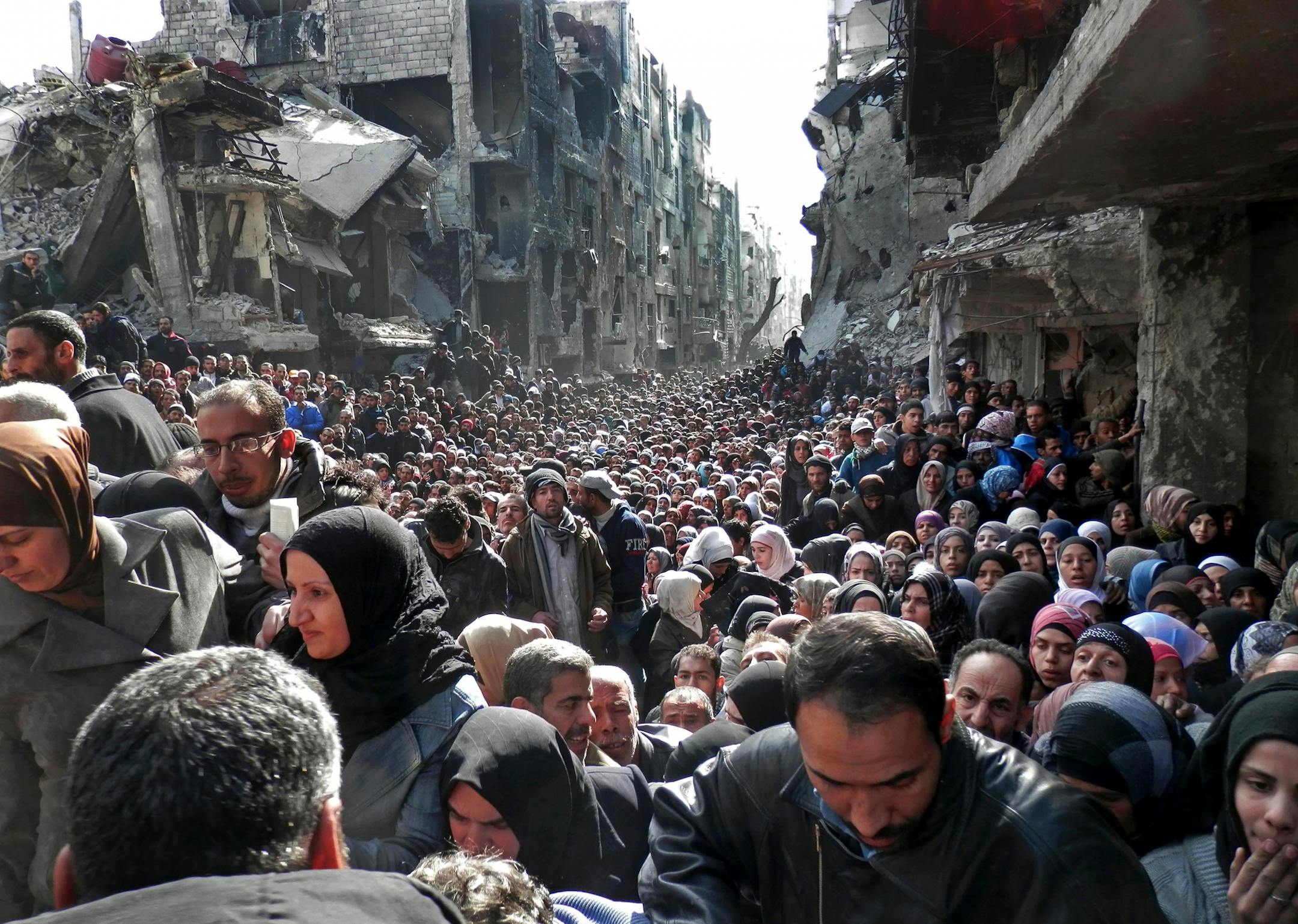 FOR USE AS DESIRED, YEAR END PHOTOS - FILE - This picture taken on Jan. 31, 2014, and released by the UNRWA, shows residents of the besieged Palestinian camp of Yarmouk, queuing to receive food supplies, in Damascus, Syria. A United Nations official called on warring sides in Syria to allow aid workers to resume distribution of food and medicine in a besieged Palestinian district of Damascus. The call comes as U.N. Secretary General Ban Ki-Moon urged Syrian government to authorize more humanitar