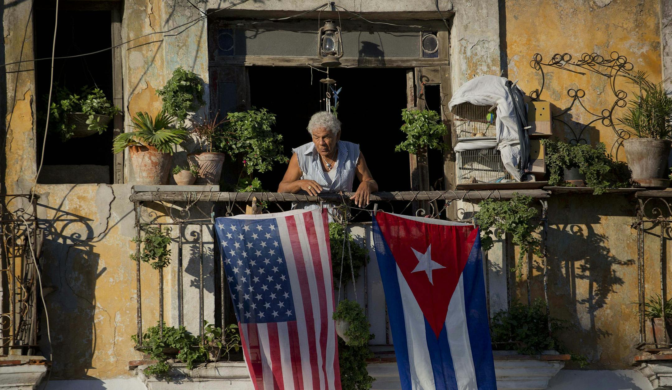 FILE - In this Dec. 19, 2014 file photo, Javier Yanez stands on his balcony decorated with U.S. and Cuban flags in Old Havana, Cuba. Roughly 45,000 Cubans are expected to travel from South and Central American countries to the Texas and California borders with Mexico this year. With thousands more sailing across the Florida Straits, 2015 may witness the biggest outflow of Cubans since the 1980 Mariel boat lift hauled 125,000 people across the Florida Straits. (AP Photo/Ramon Espinosa, File) ORG