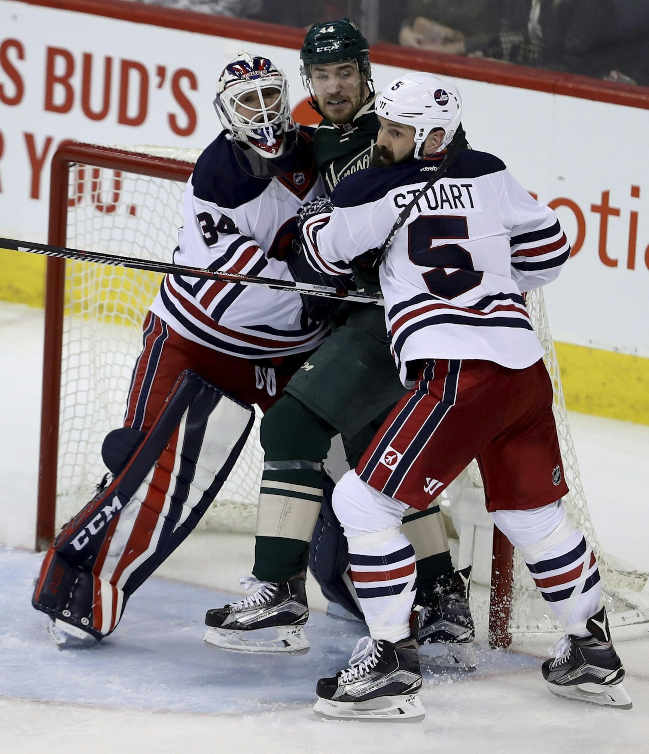 Winnipeg Jets goaltender Michael Hutchinson (34) and teammate Mark Stuart (5) battle with Minnesota Wild's Tyler Graovac during the third period of an NHL hockey game in Winnipeg, Manitoba, Sunday, March 19, 2017.