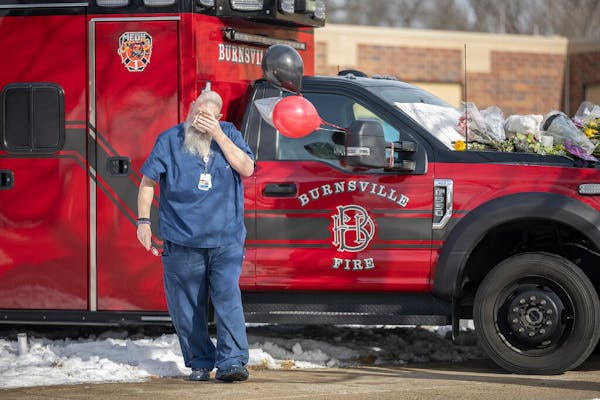 A health care professional weeps on a paramedic vehicle that has become one of three memorials in front of the Burnsville Police Department in Burnsvi