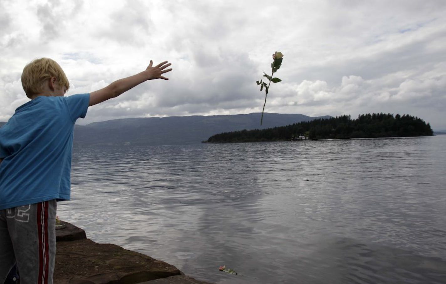 A young boy threw a rose into the lake opposite to the island of Utoya, Norway, a couple of days after two attacks, a shooting massacre on the island and a bombing in central Oslo killed nearly 80 people. Anders Behring Breivik is accused in the crimes.