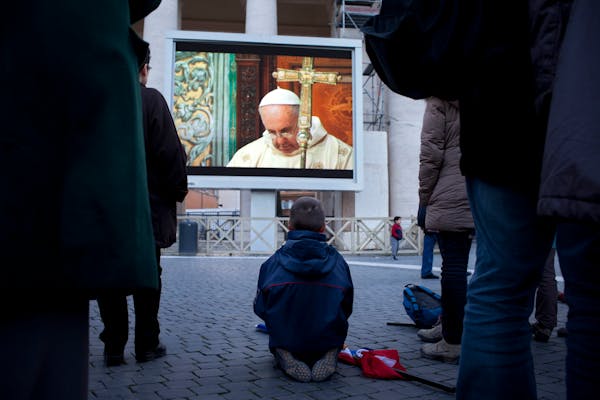 People watch Pope Francis on a giant screen in St. Peter's square as he celebrates his inaugural Mass with cardinals inside the Sistine Chapel, at the