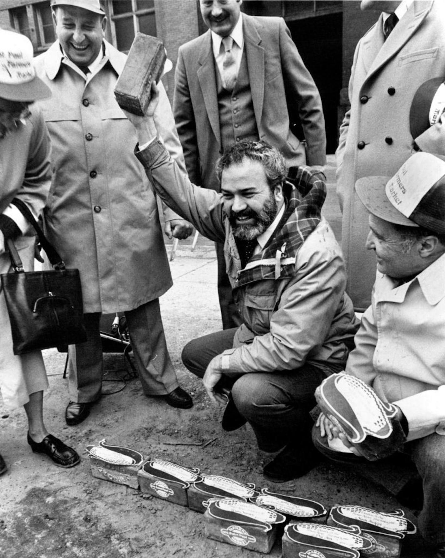 April 12, 1982: St. Paul Mayor George Latimer waves a brick, one of the first to be symbolically placed on the site of the new farmers market at the corner of Fifth & Broadway in St. Paul. Among those attending were Peter Costa, president of the St. Paul Growers Assn., at left (directly to the left of the raised brick), and City Councilman Victor Tedesco, lower right. Art Hager, Minneapolis Star Tribune