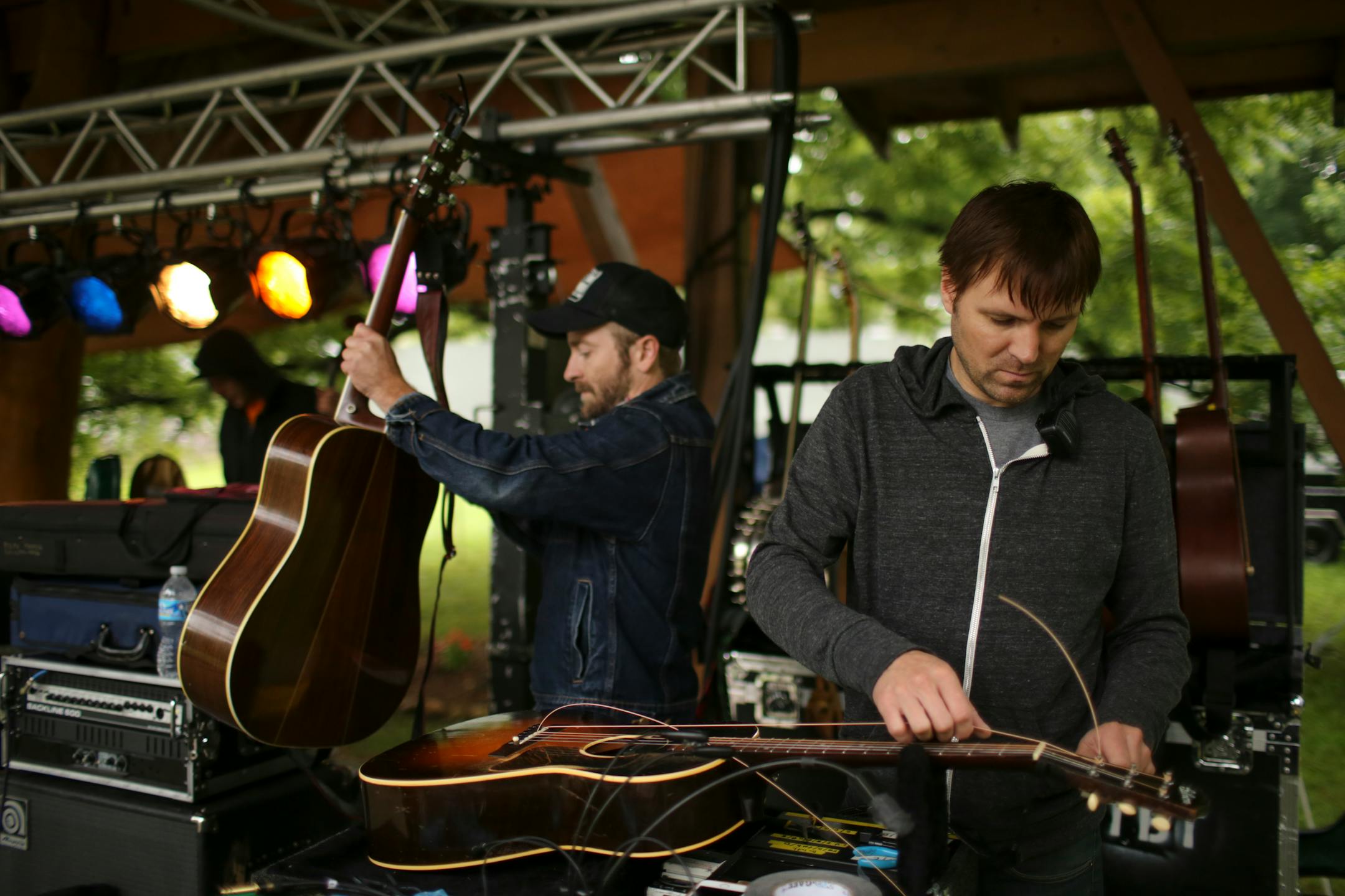 Dave Simonett grabbed his guitar to begin sound check for their show while string tech Matt Feirn restrung a guitar at the side of the stage in Black Mountain, N.C., in August 2014.