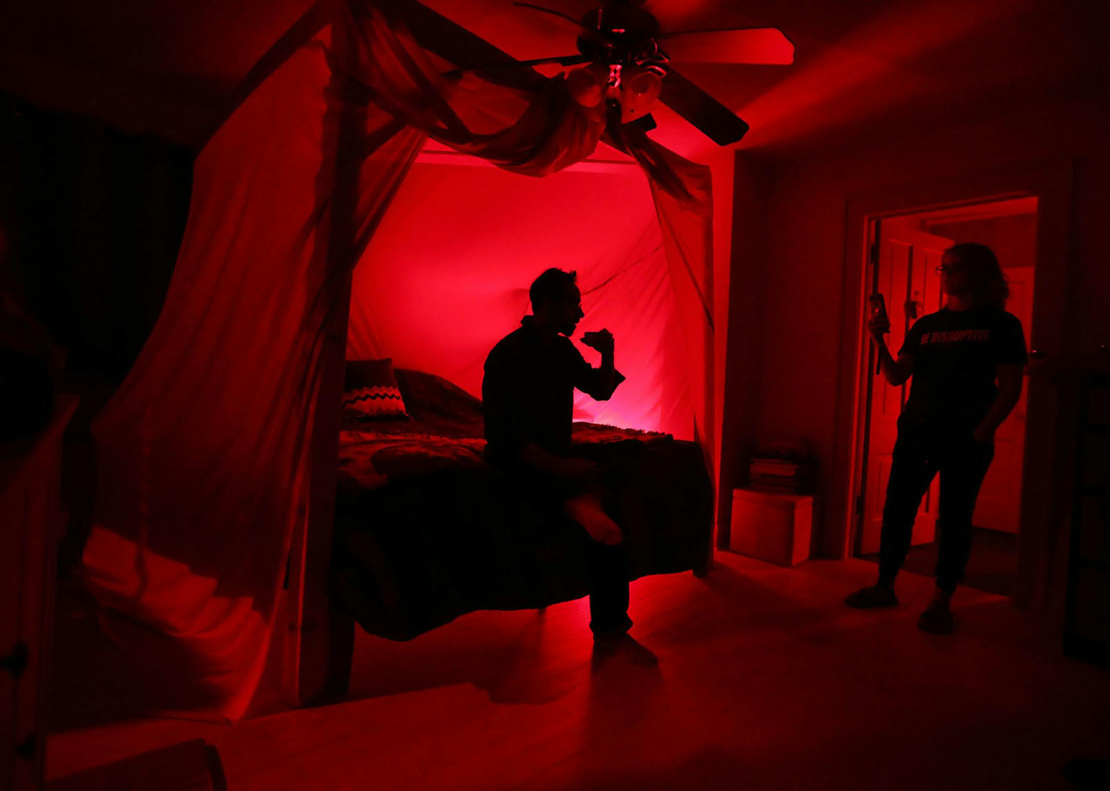 Biohackers Thaddeus Owen and Heidi Sime in the bedroom of their home with their bed in a faraday, a silver mesh cage meant to block out microwaves and bathed in red light.