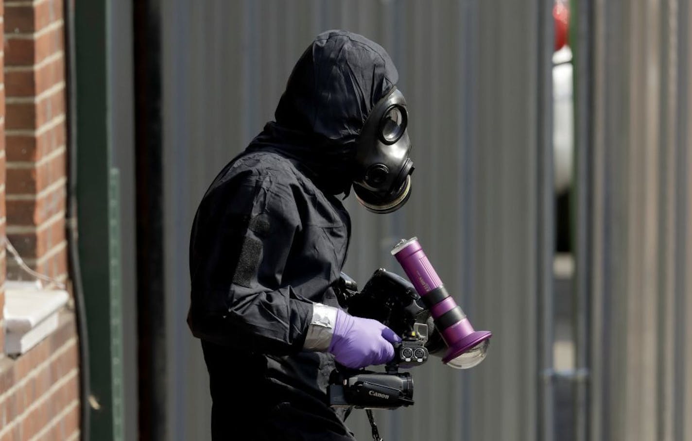 A specialist team member in a police protective suit leaves the front entrance of John Baker House for homeless people on Rollestone Street in Salisbury, England, Friday, July 6, 2018. British police are scouring sections of Salisbury and Amesbury in southwest England, searching for a container feared to be contaminated with traces of the deadly nerve agent Novichok.