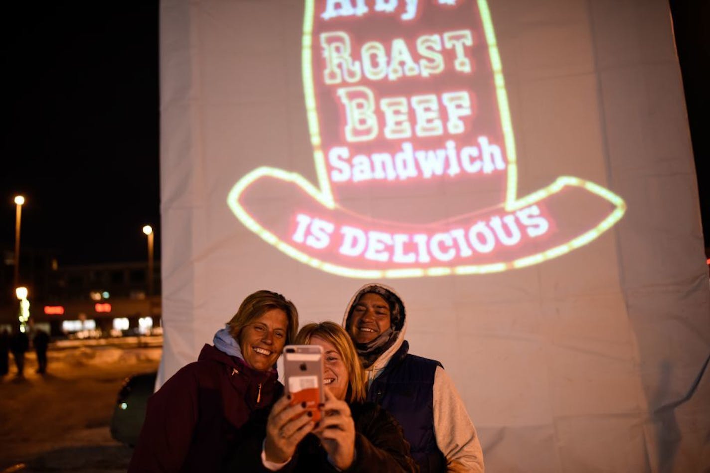 From left, Karen DeVries, of Minneapolis, Lisa Schlepuetz, of Apple Valley and Mike Butler, of Bloomington, posed for a selfie in front of a projected Arby's sign that was placed in the location of the old Arby's sign before Friday night's vigil. .