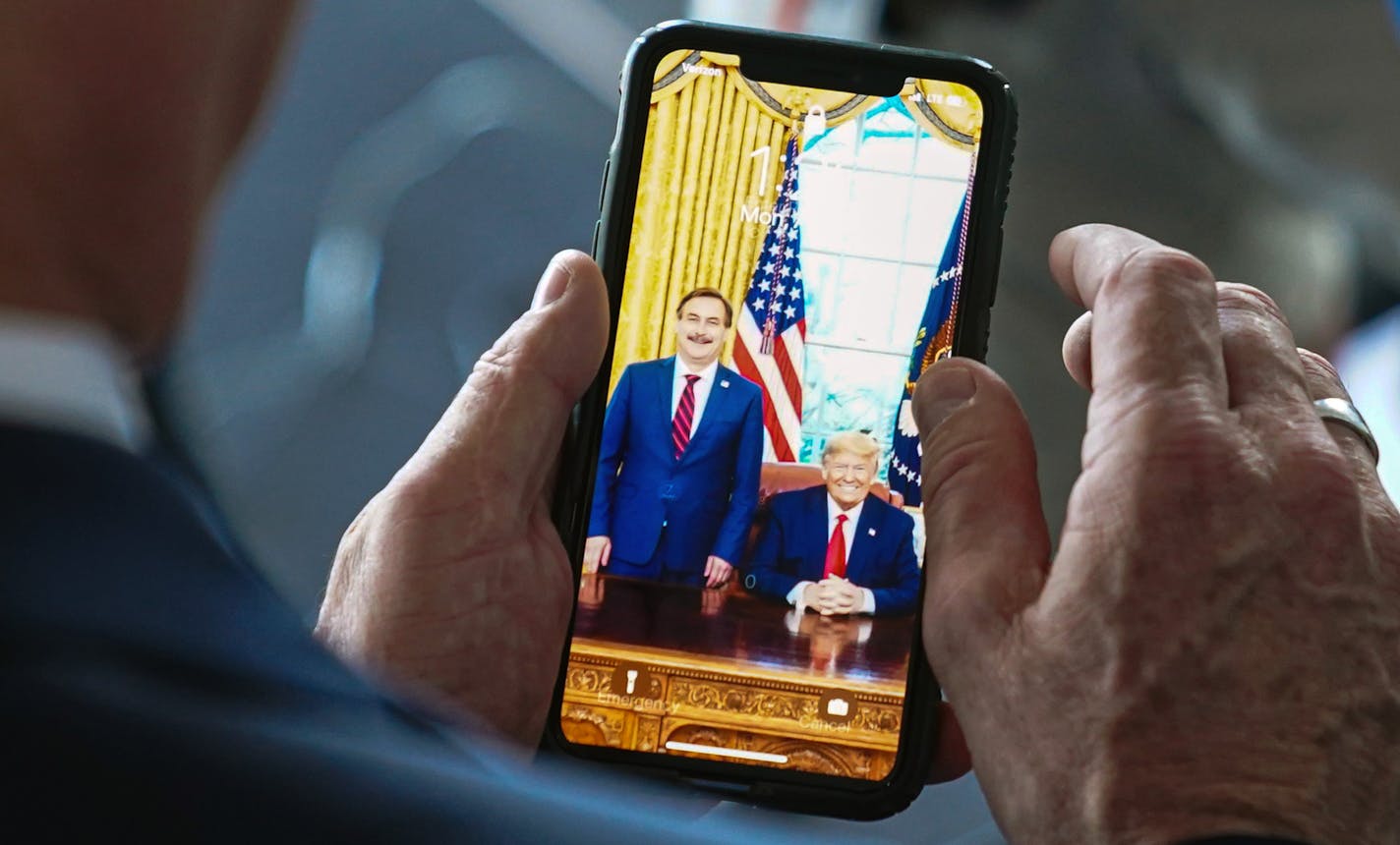 Mike Lindell showed his cell phone to Jason Lewis as they waited for President Donald Trump to arrive in Mankato.  Lindell's background screen was a photo with President Trump in the Oval Office.