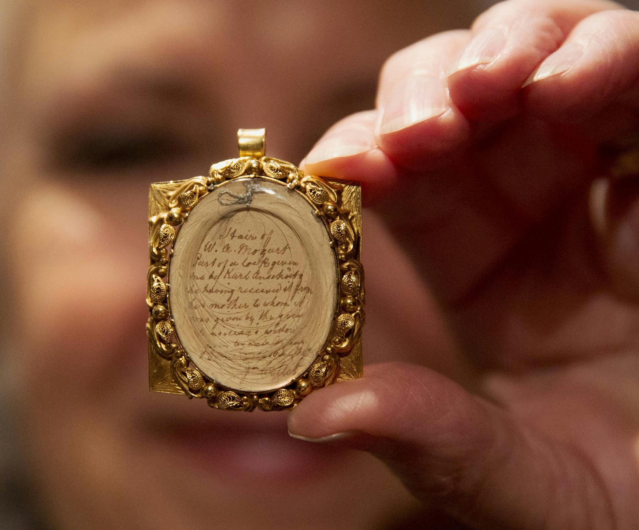 Gallery assistant Sandra Handley poses for photographs with a lock of Wolfgang Amadeus Mozart's hair, contained in a 19th-century gilt locket at the Sotheby's auction house in London, Tuesday, May 26, 2015. The lock of hair is estimated to fetch 10,000 to 12,000 pounds ($15,383 to $18,459, euro14,109 to 16,931) as part of the Music, Continental and Russian Books and Manuscripts auction on Thursday May 28 in London. (AP Photo/Matt Dunham)