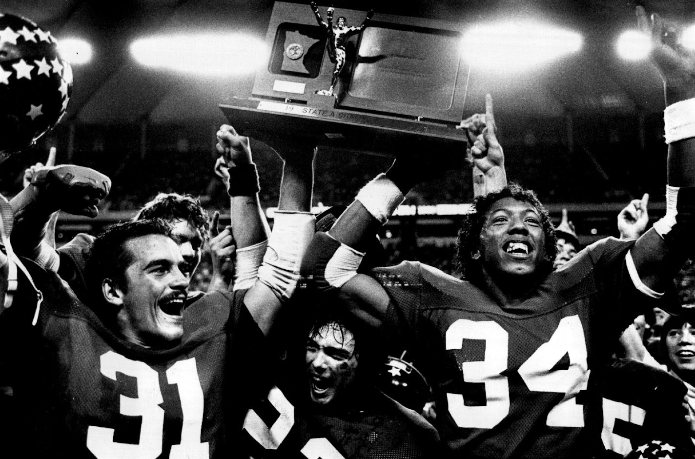 November 25, 1982 Senior co-captains Joe Novak, left, and Tracy Martin, right, held up their first-place trophy, while Doug Jennrich, center, cheered Saturday after Brooklyn Center beat East Grand Forks win the state Class A title at the Metrodome. John Croft, Minneapolis Star Tribune