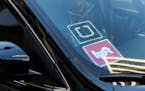 FILE - In this Tuesday, Jan. 12, 2016, file photo, a driver displaying Lyft and Uber stickers on his front windshield drops off a customer in downtown
