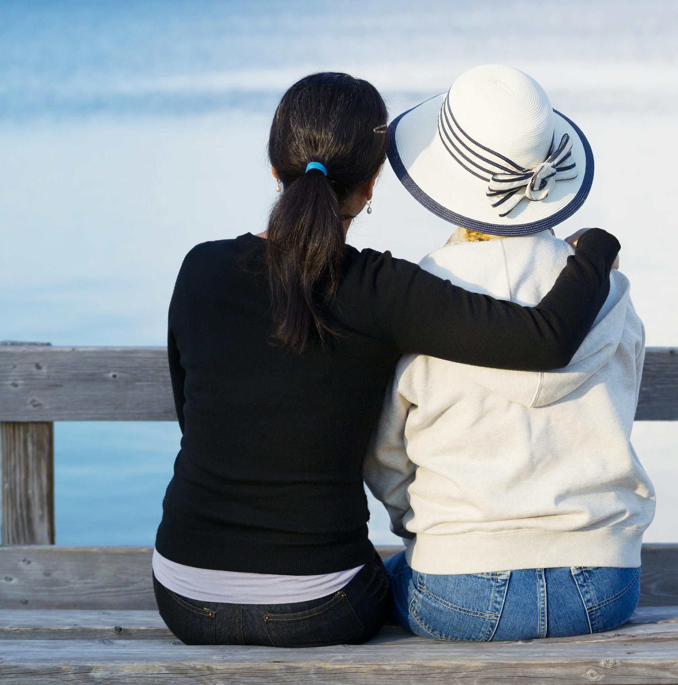 Closeup of mother and mature daughter siting on wooden bench while looking at the lake. istock