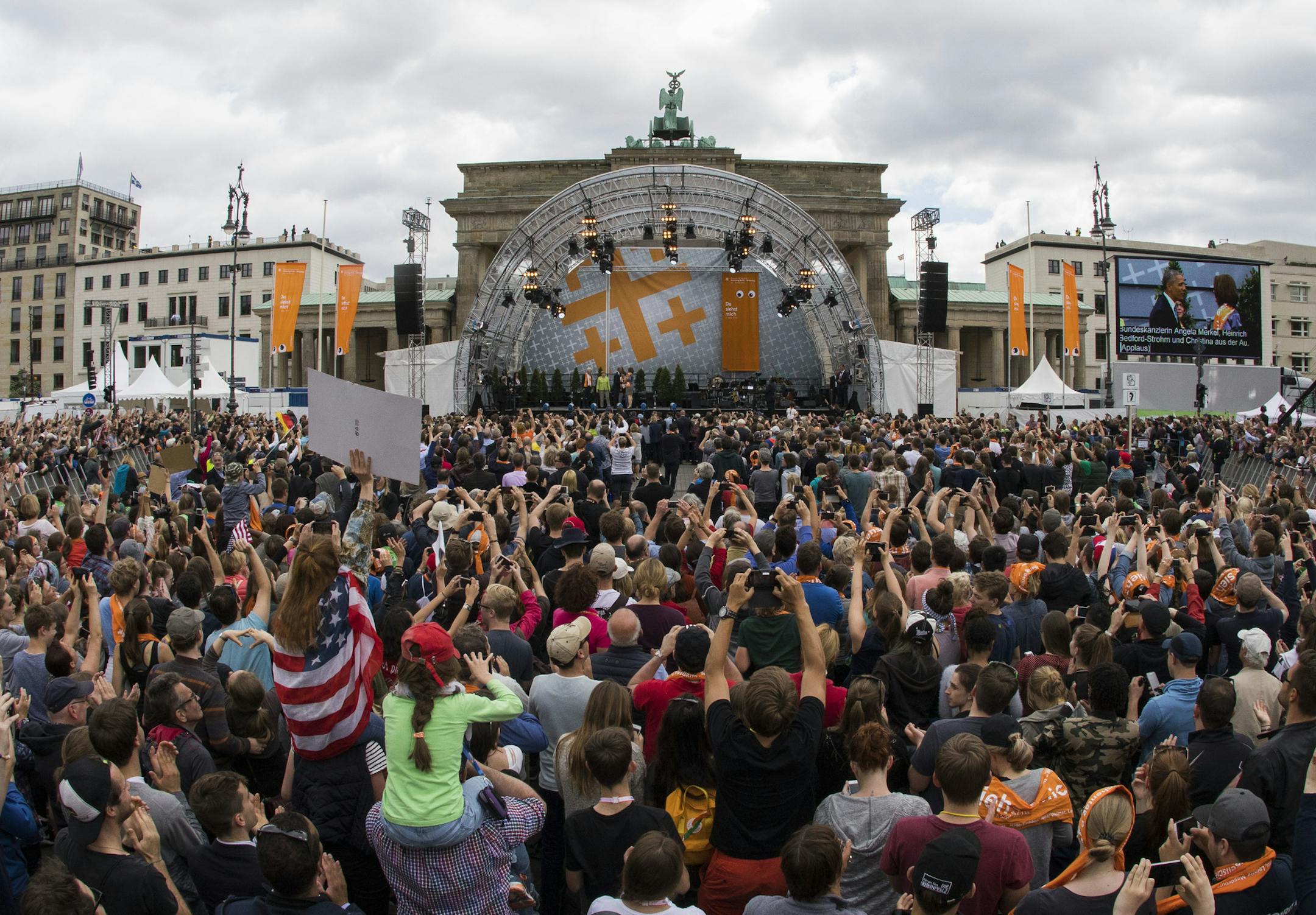 In this photo taken with a 15mm fish eye lens people gather in front of Brandenburg Gate as former U.S. President Barack Obama and German Chancellor Angela Merkel enter the stage for a discussion event on democracy and global responsibility at a Protestant conference in Berlin, Germany, Thursday, May 25, 2017, when Germany marks the 500th anniversary of the Reformation. (AP Photo/Gero Breloer)