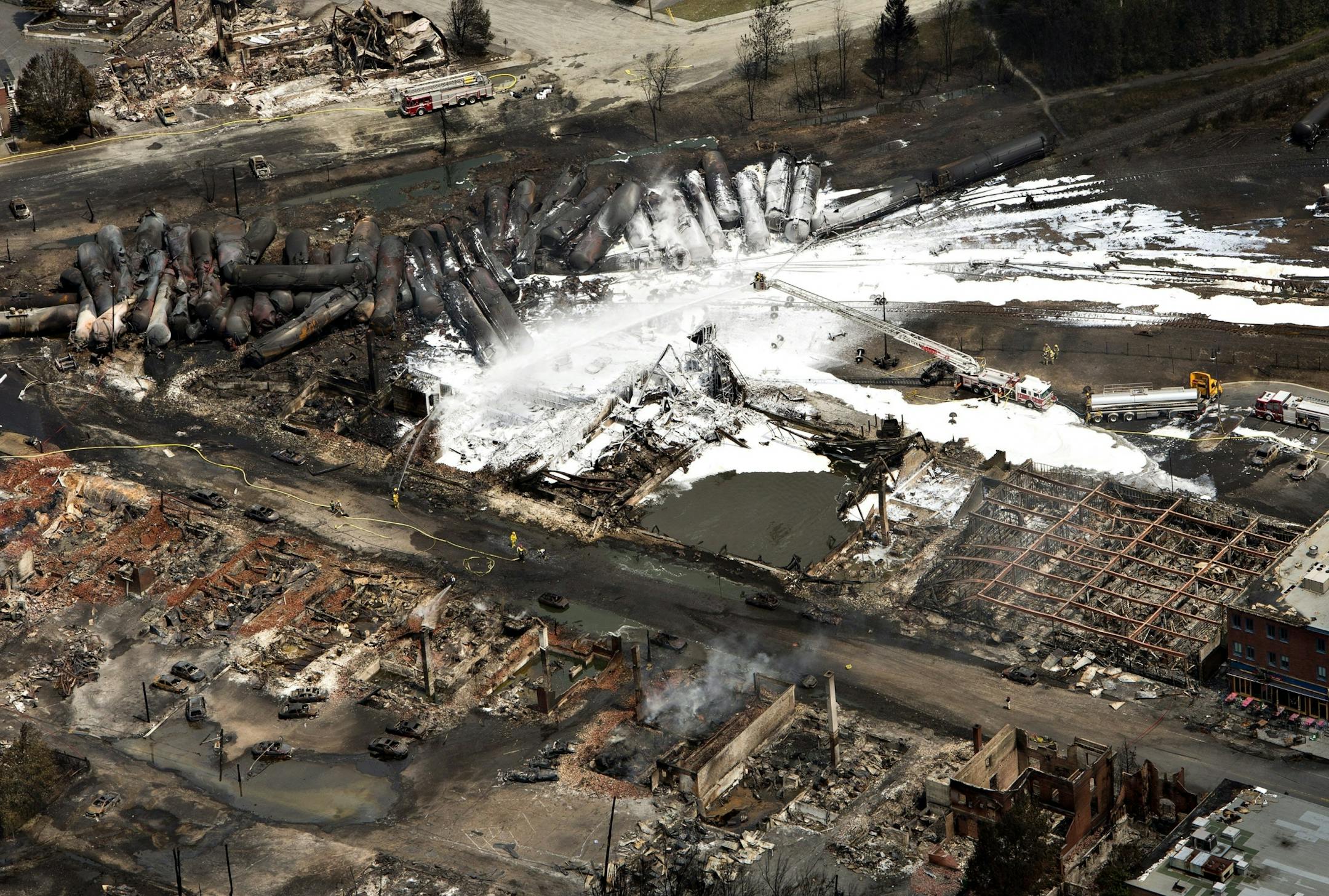 The downtown core lays in ruins as fire fighters continue to water smoldering rubble Sunday, July 7, 2013, in Lac Megantic, Quebec, after a train derailed ignited tanker cars carrying crude oil. The derailment Saturday caused explosions and fires that destroyed the downtown district.