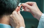 Doctor inserting hearing aid in senior's ear.