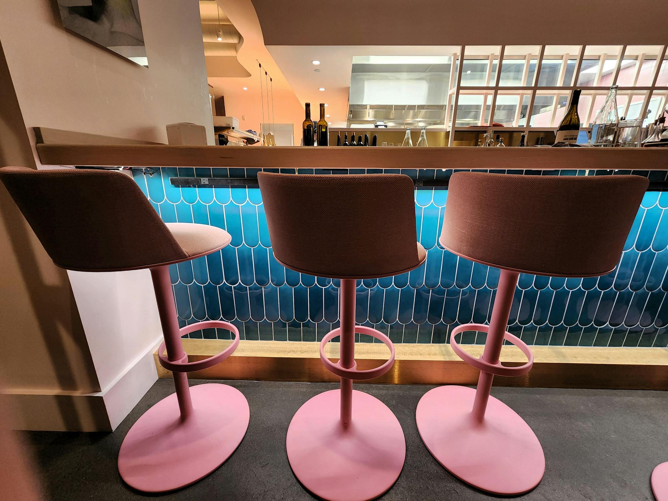 Bubblegum pink barstools against an ocean blue tile wall under the bar