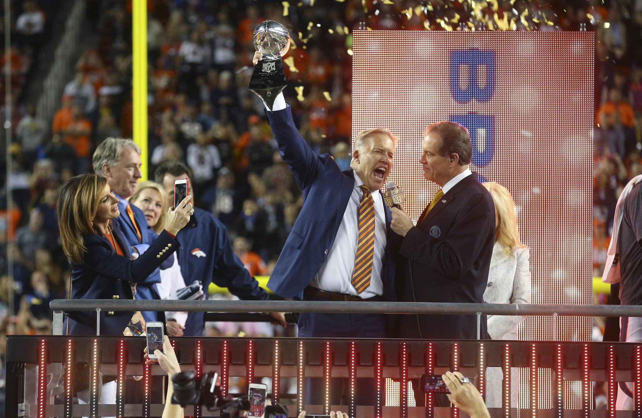 While interviewed by sportscaster Jim Nance, John Elway, general manager of the Denver Broncos and once quarterback for the team, celebrates with the Vince Lombardi trophy after beating the Carolina Panthers in Super Bowl 50 at Levi's Stadium in Santa Clara, Calif., Feb. 7, 2016. (Chang W. Lee/The New York Times)