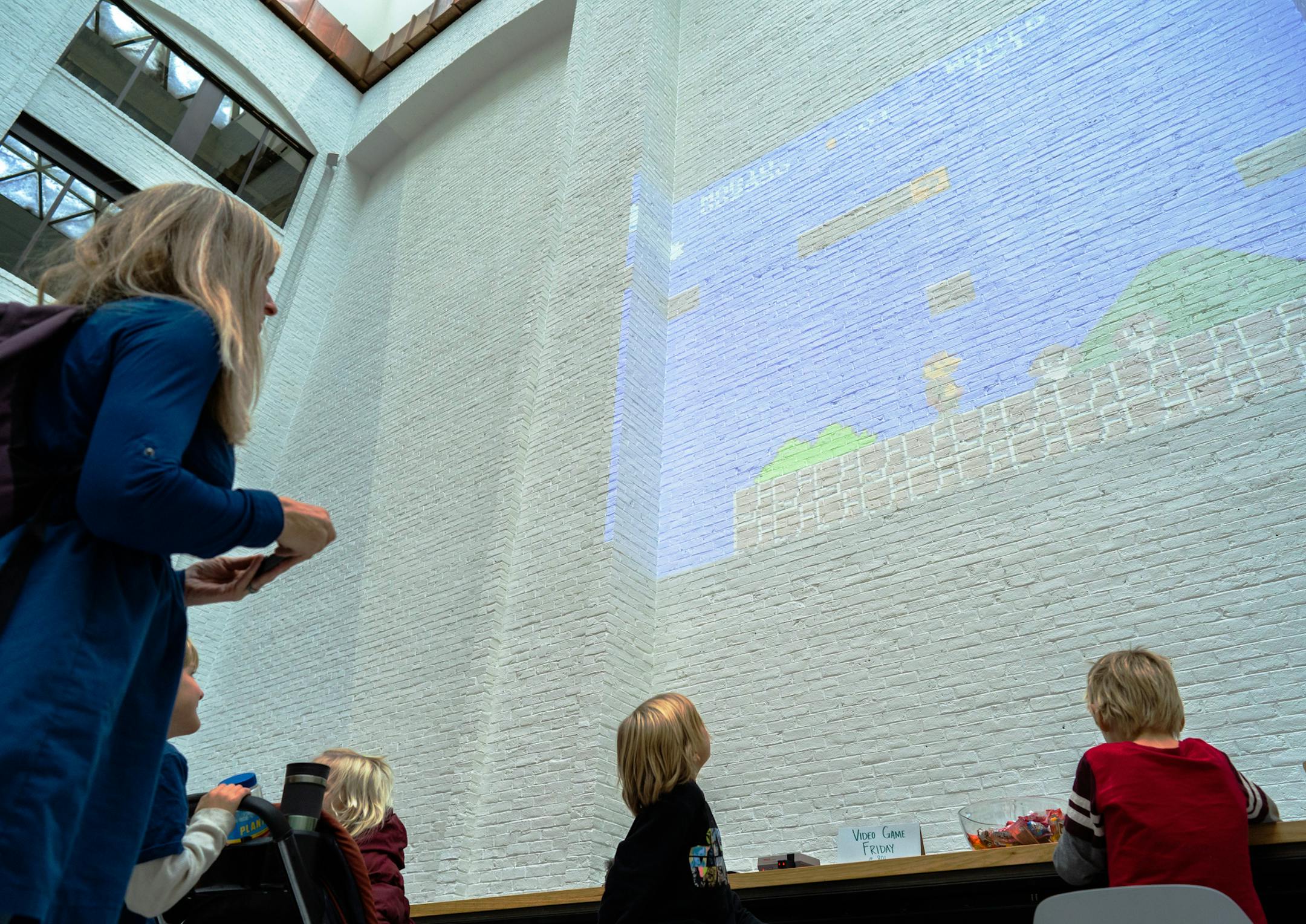 Emily Reese played a round of Mario while her children watched. The family was touring downtown on a day trip from Goodhue, Minn. ] MARK VANCLEAVE • mark.vancleave@startribune.com * The Musicant Group projected classic Nintendo games in the atrium of the 801 Marquette building in downtown Minneapolis as part of their programming for the space on Friday, Nov. 9, 2018.