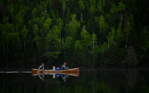 Tony Jones, left, his yellow Lab Crosby, and Bob Timmons paddled over a still Mountain Lake on June 14 toward their portages to Moose Lake.