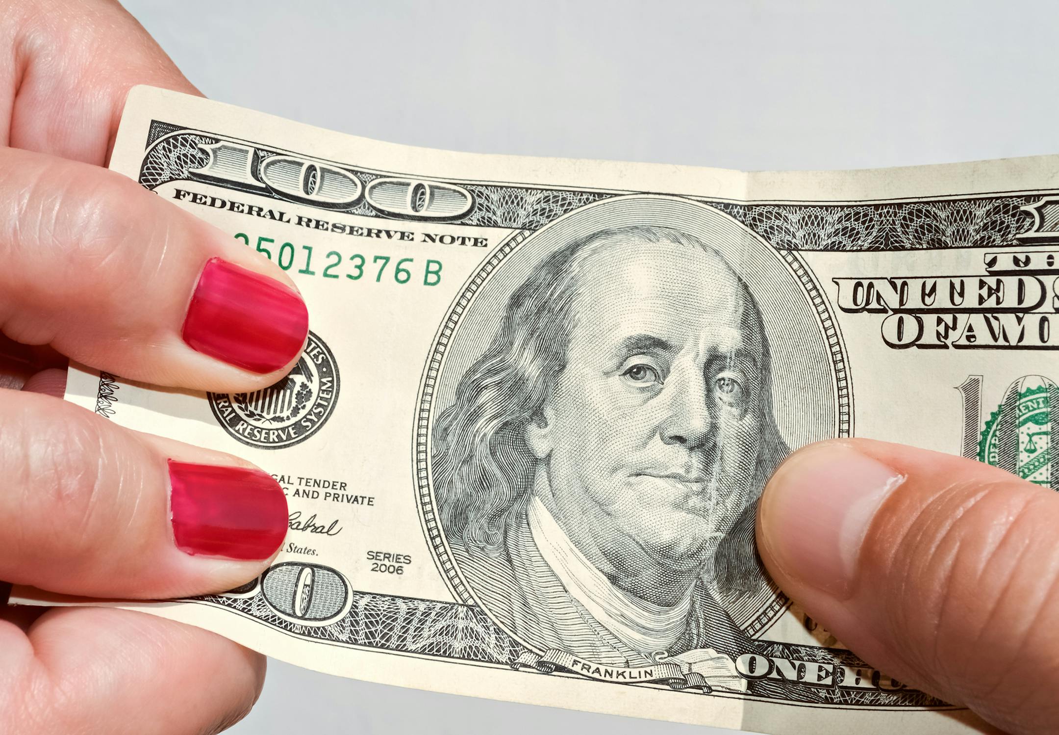 Closeup of hands pulling a hundred dollar banknote