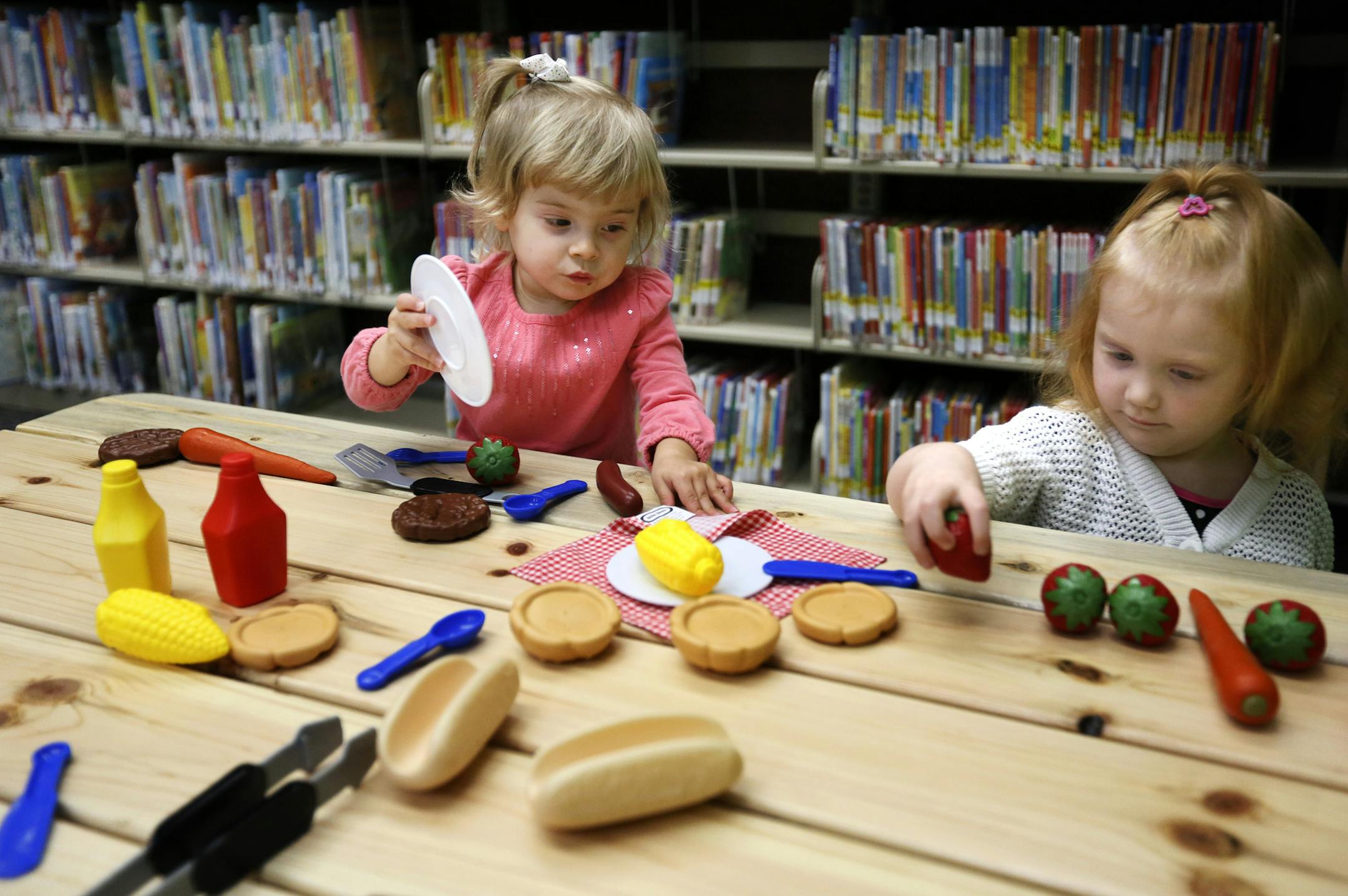 Minnesota's Children Museum is behind a new "Smart Play Spot" at the Anoka County Library in Fridley which includes a play bus and farmer's market. It was funded largely by the State of Minnesota, Clean Water, Land and Legacy Amendment, Arts and Cultural Heritage Fund. This kind of 3D learning experience is part of the evolution of libraries from book depot to hands-on learning lab. Here, 2-year-old's Audrey Anderson and Hannah Henderson prepare a picnic lunch after shopping at the farmers marke