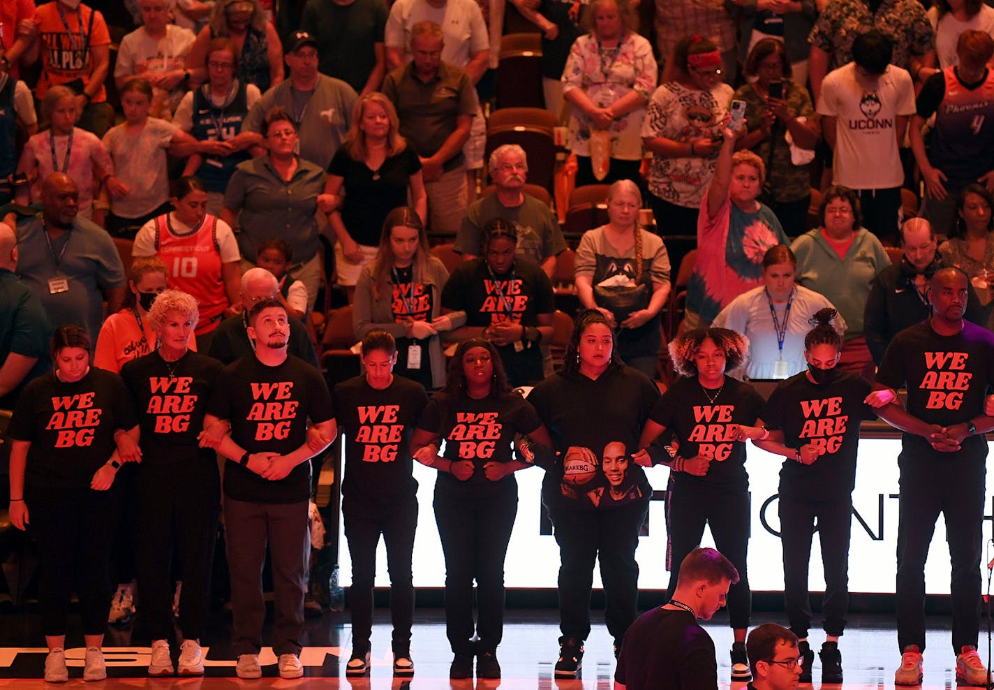 Coaching staff link arms as players with the Connecticut Sun and Phoenix Mercury stand at center court for 42 seconds in honor of Phoenix Mercury center Brittney Griner at a WNBA basketball game Thursday, Aug. 4, 2022, in Uncasville, Conn. Griner was convicted Thursday in Russia of drug possession and smuggling and was sentenced to nine years behind bars. (Sarah Gordon/The Day via AP)