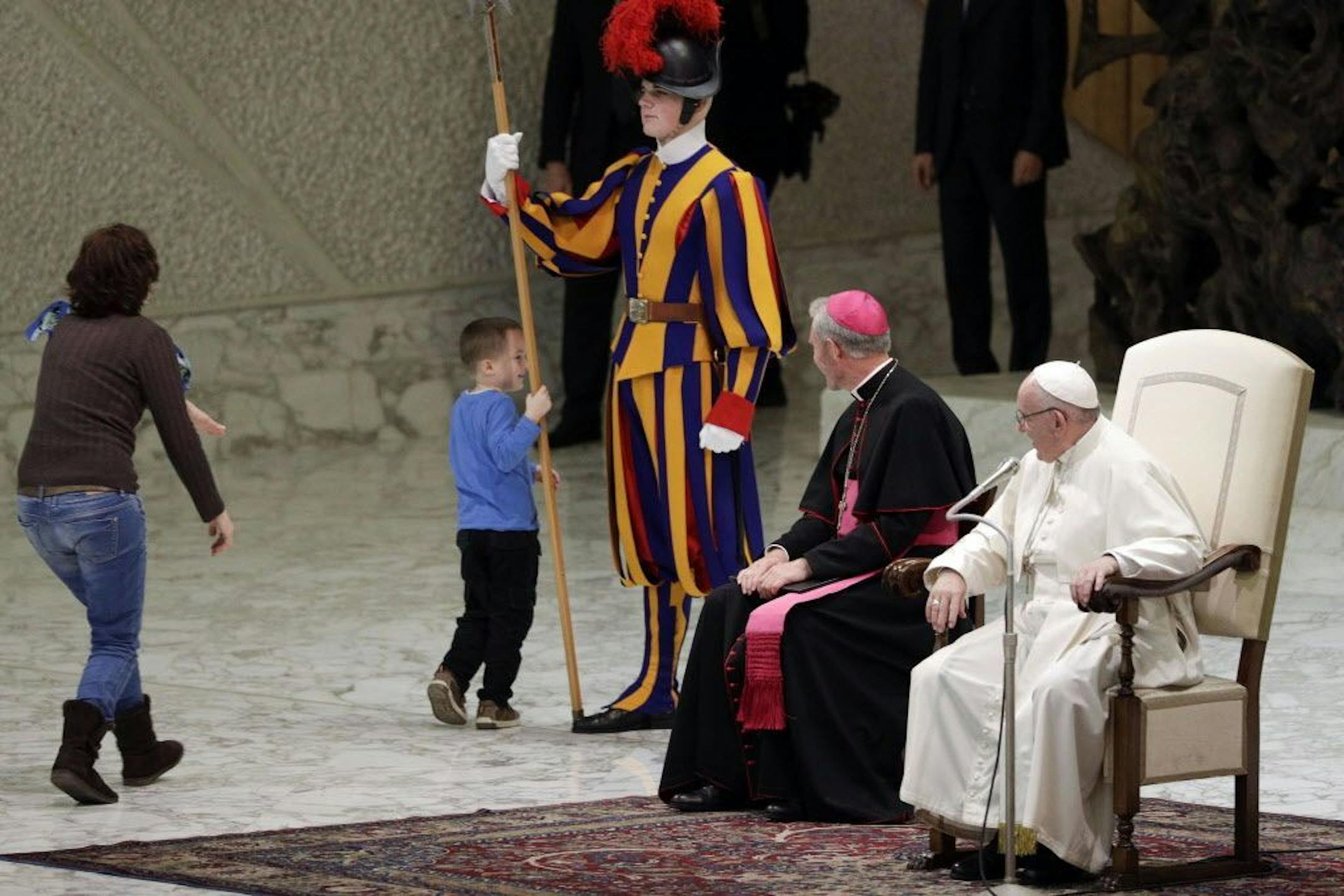 A child plays with a Swiss guard in the Paul VI Hall at the Vatican, Wednesday, Nov. 28, 2018. Pope Francis has praised the freedom, albeit undisciplined, of a hearing impaired child who climbed onto the stage during his general audience to play. The Swiss Guards and Vatican gendarmes stood by Wednesday and gamely let the young boy run around Francis as monsignors read out his catechism lesson in various languages in the Vatican audience hall.
