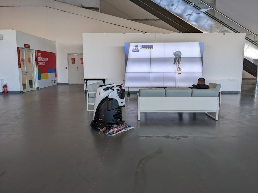 A couple of sweepers at the Olympic media center: A curler on TV and a robot in the room.