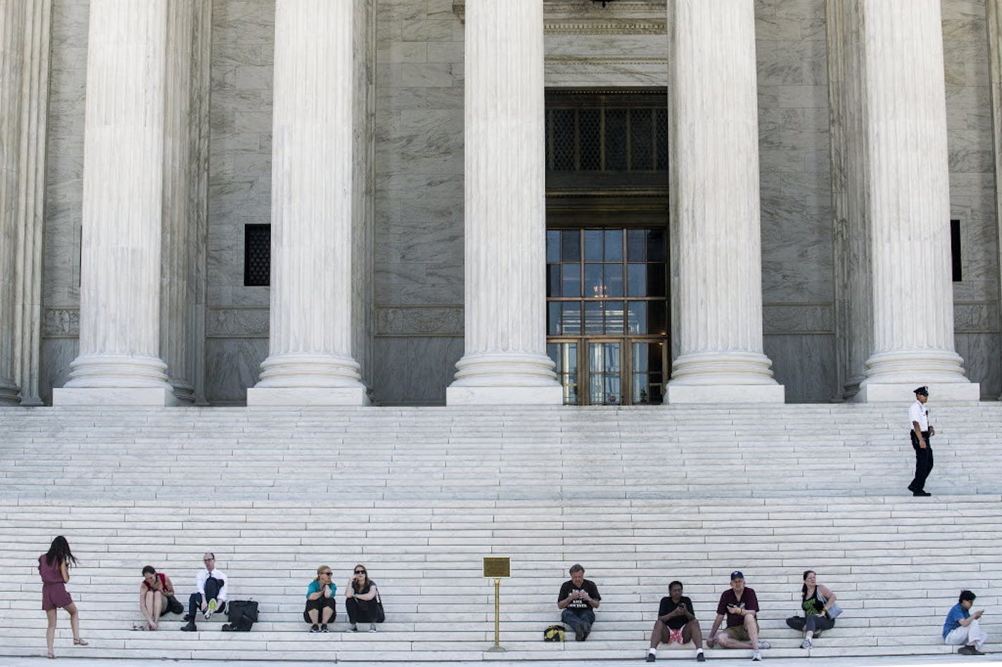 Visitors sit on the steps of the U.S. Supreme Court building on Capitol Hill in Washington, where justices issued decisions Thursday on several cases.