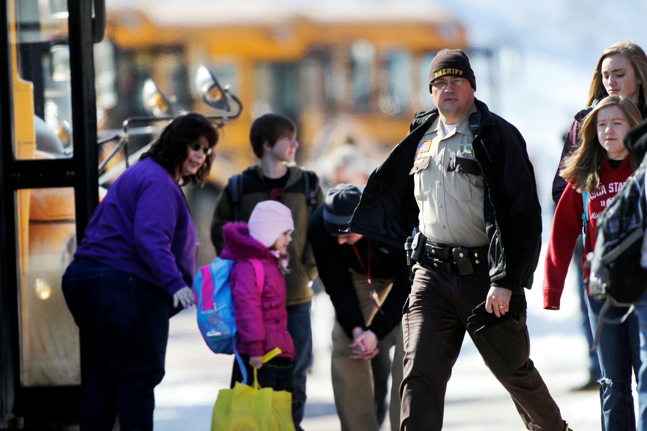 Students headed to buses after school had been cancelled for the day, past a law enforcement officer after lockdown had been lifted Wednesday, March 20, 2013, at New Prague Middle School in New Prague, Minn.