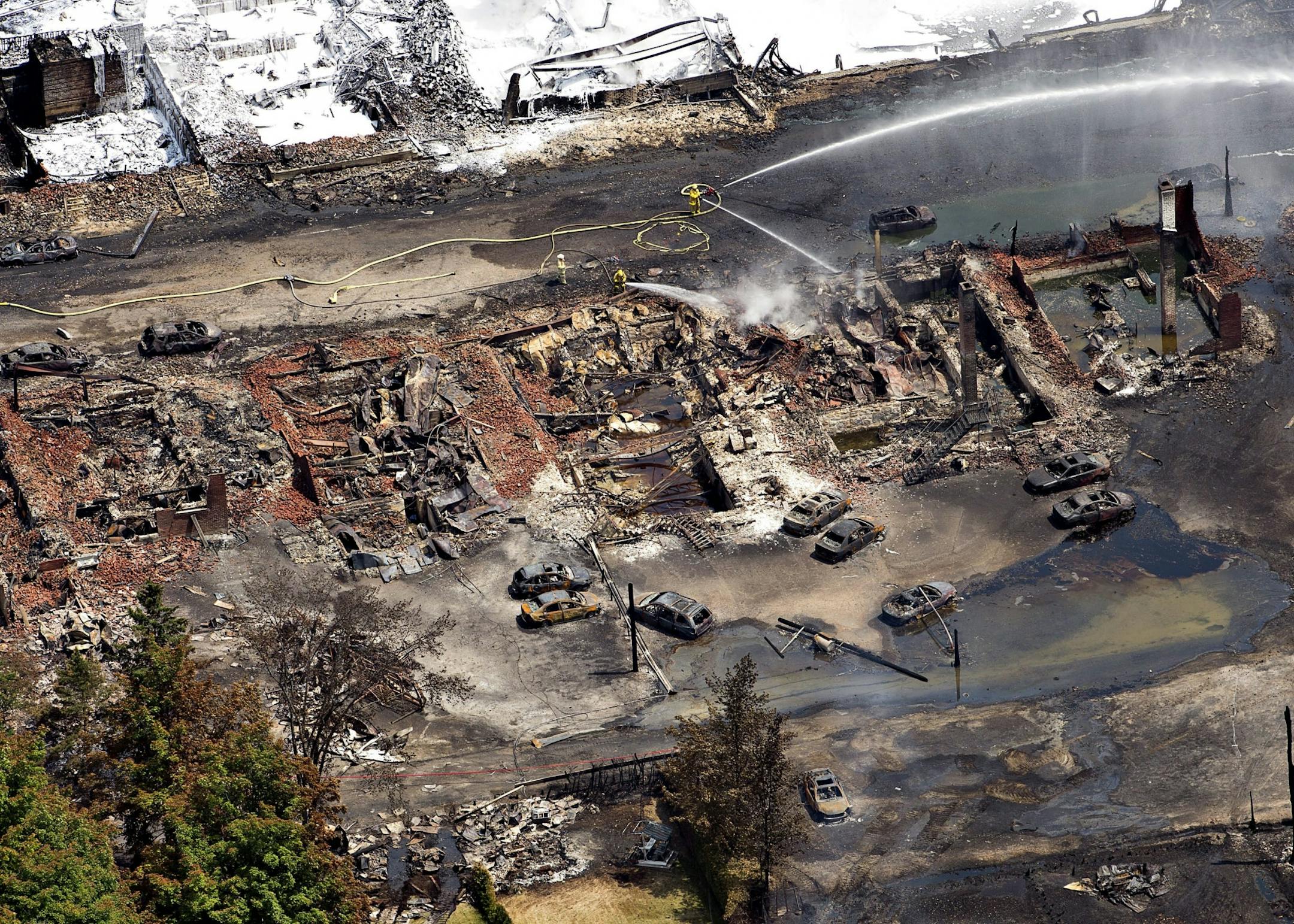 The downtown core lays in ruins as fire fighters continue to water smoldering rubble Sunday, July 7, 2013 in Lac Megantic, Quebec after a train derailed ignited tanker cars carrying crude oil. More bodies were recovered Sunday in the devastated town of Lac Megantic, raising the death toll to at least five after a runaway train derailed, igniting explosions and fires that destroyed the downtown district. With dozens of people reported missing, authorities feared they could find more bodies once t