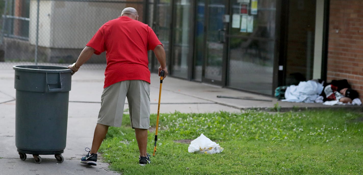 Salvador Pacheco, director of facility and security services at Minnesota Indian Women's Resource Center, picks up trash and discarded syringes as nearby a man sleeps outside the center Thursday, June 20, 2019, in Minneapolis, MN. Discarded needles and other signs of drug use are personal to Pacheco who lives in apartment at MIWCR near one of his daughters and two grand children and has family members fighting substance abuse. "They're people," he said. "They're somebody's son, mom, somebody's d