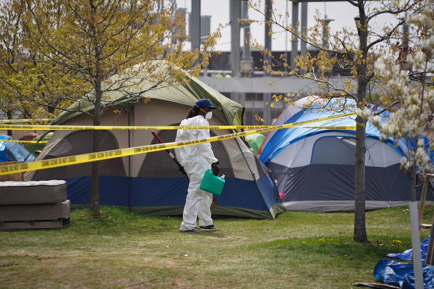 A small camp of about a dozen tents along Hiawatha Avenue has swelled to more than 100 homeless men and women. Crews wearing protective Tyvek suits cleaned debris Thursday.