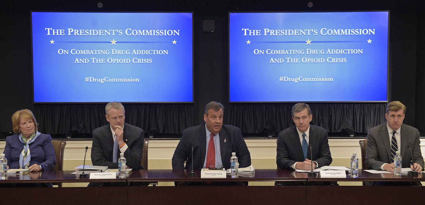 New Jersey Gov. Chris Christie, center, chairman of the President's Commission on Combating Drug Addiction and the Opioid Crisis, peaks at the beginning of the first meeting of the commission on combating drug addiction and the opioid crisis, Friday, June 16, 2017, in the Eisenhower Executive Office Building at the White House complex in Washington. From left are , Dr. Bertha K. Madras, a Harvard Medical School professor who specializes in addiction biology, Massachusetts Gov. Charlie Baker, Chr