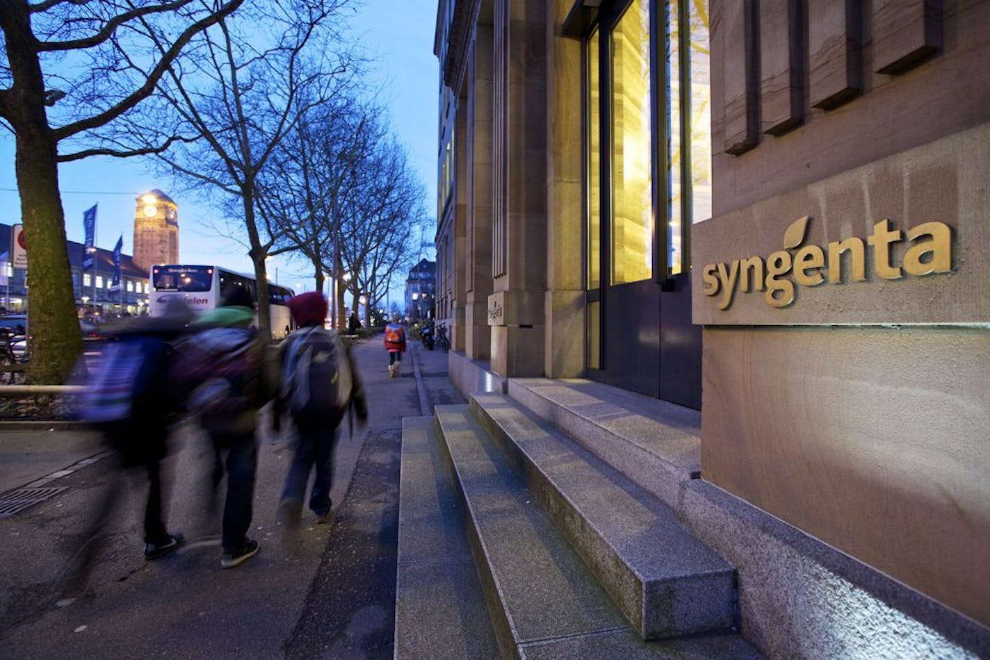 Pedestrians walk past the entrance to Syngenta AG's headquarters in Basel, Switzerland, on Wednesday, Feb. 5, 2014. Syngenta, the world's largest maker of crop chemicals, reported profit that missed analysts' estimates and Chief Executive Officer Mike Mack pledged to cut $1 billion in costs by 2018 to boost efficiency. Photographer: Gianluca Colla/Bloomberg