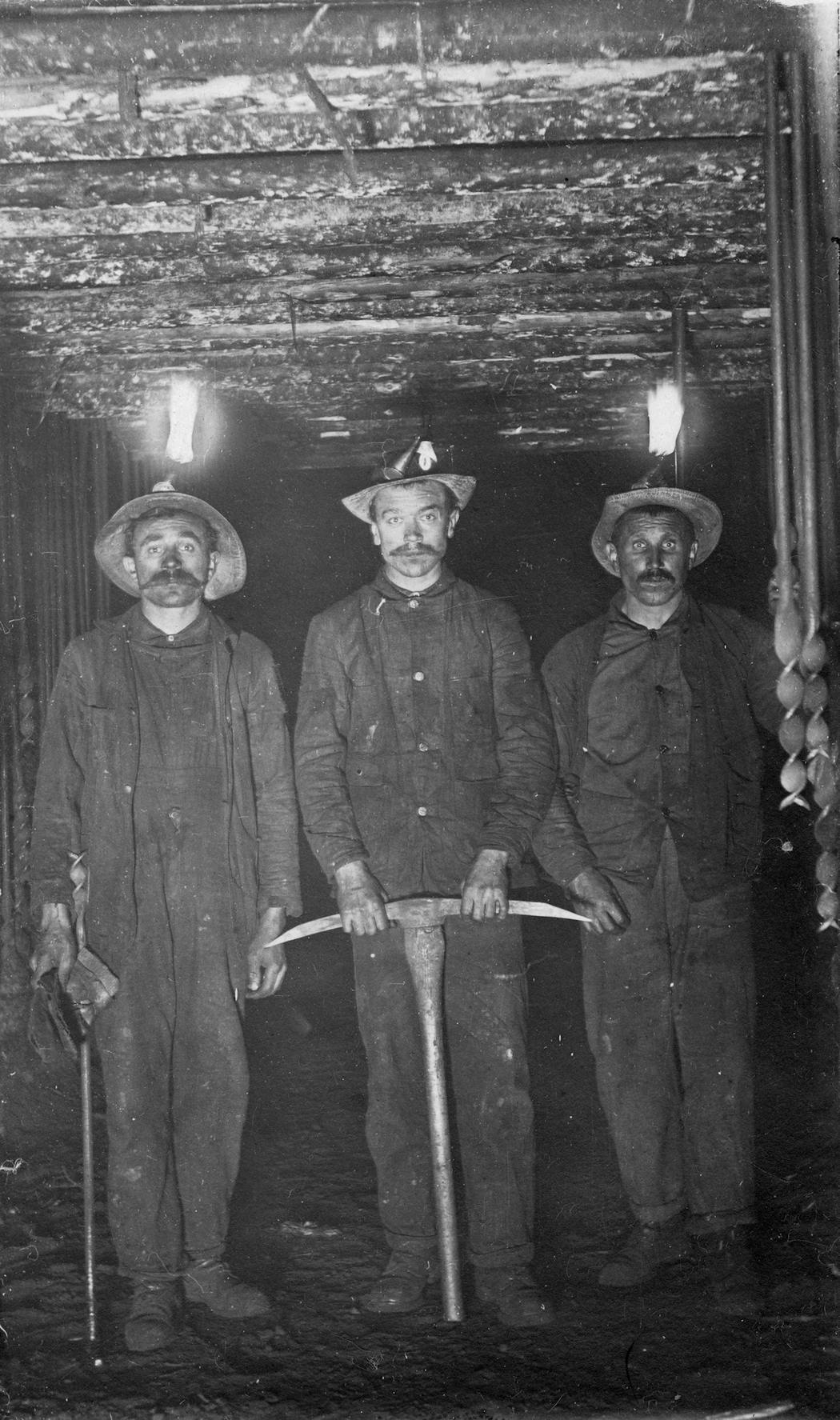 Underground miners in a shaft in the early 1900s, wearing leather helmets and candles.