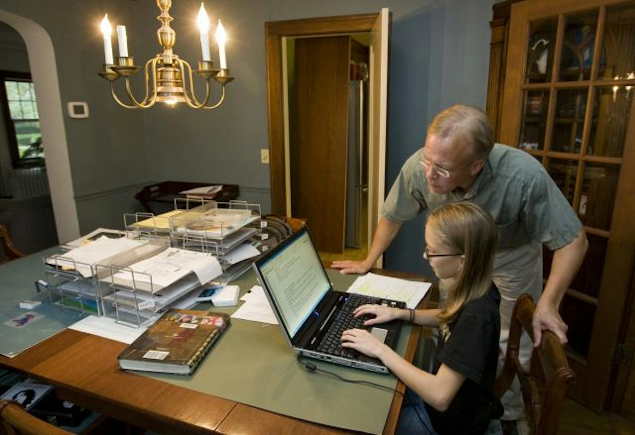 Scott Newland repurposed the dining room table into a study area for their kids. Sixth grader Nina Newland gets a little help from dad while she types a paper on the family computer at her end of the table.