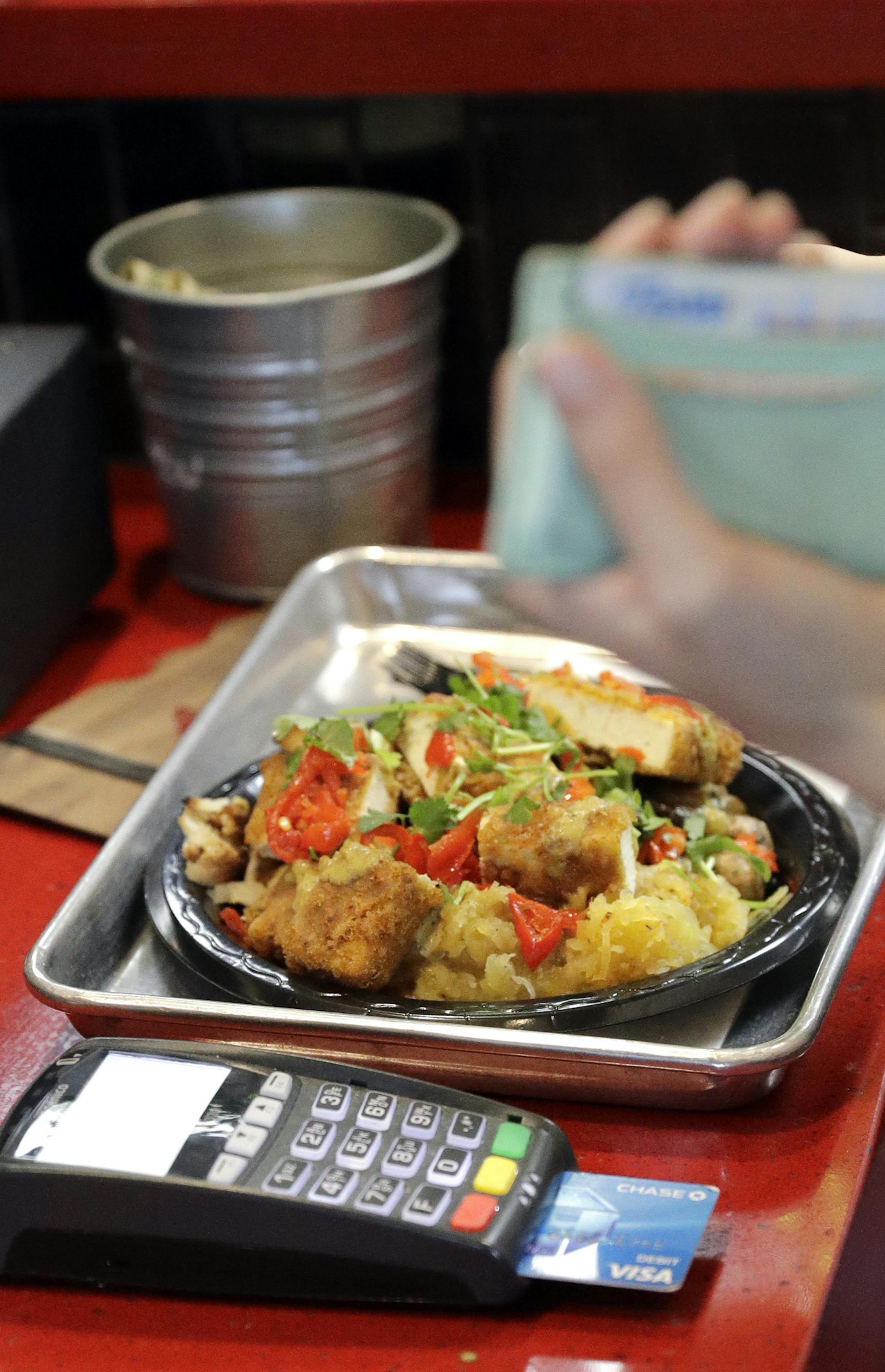 In this Tuesday, April 10, 2018, photo, a customers uses a credit card machine to pay for food at Peli Peli Kitchen in Houston. Owner Thomas Nguyen had a change of heart after transitioning one of his three Peli Peli South African fine dining restaurants and his Peli Peli Kitchen fast casual location to a no-cash policy. (AP Photo/David J. Phillip) ORG XMIT: TXDP104