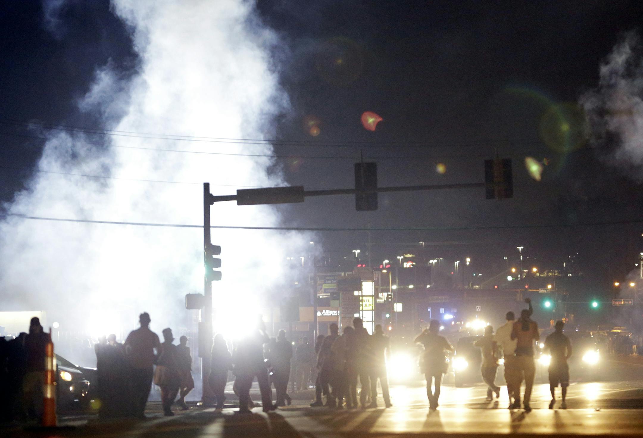 FILE - In this Monday, Aug. 18, 2014 file photo, people stand near a cloud of tear gas in Ferguson, Mo. during protests for the Aug. 9 shooting of unarmed black 18-year-old Michael Brown by a white police officer. The U.S. government agreed to a police request to shut down several miles of airspace surrounding Ferguson, even though authorities said their purpose was to keep media helicopters away during protests in August, according to recordings of air traffic control conversations obtained by