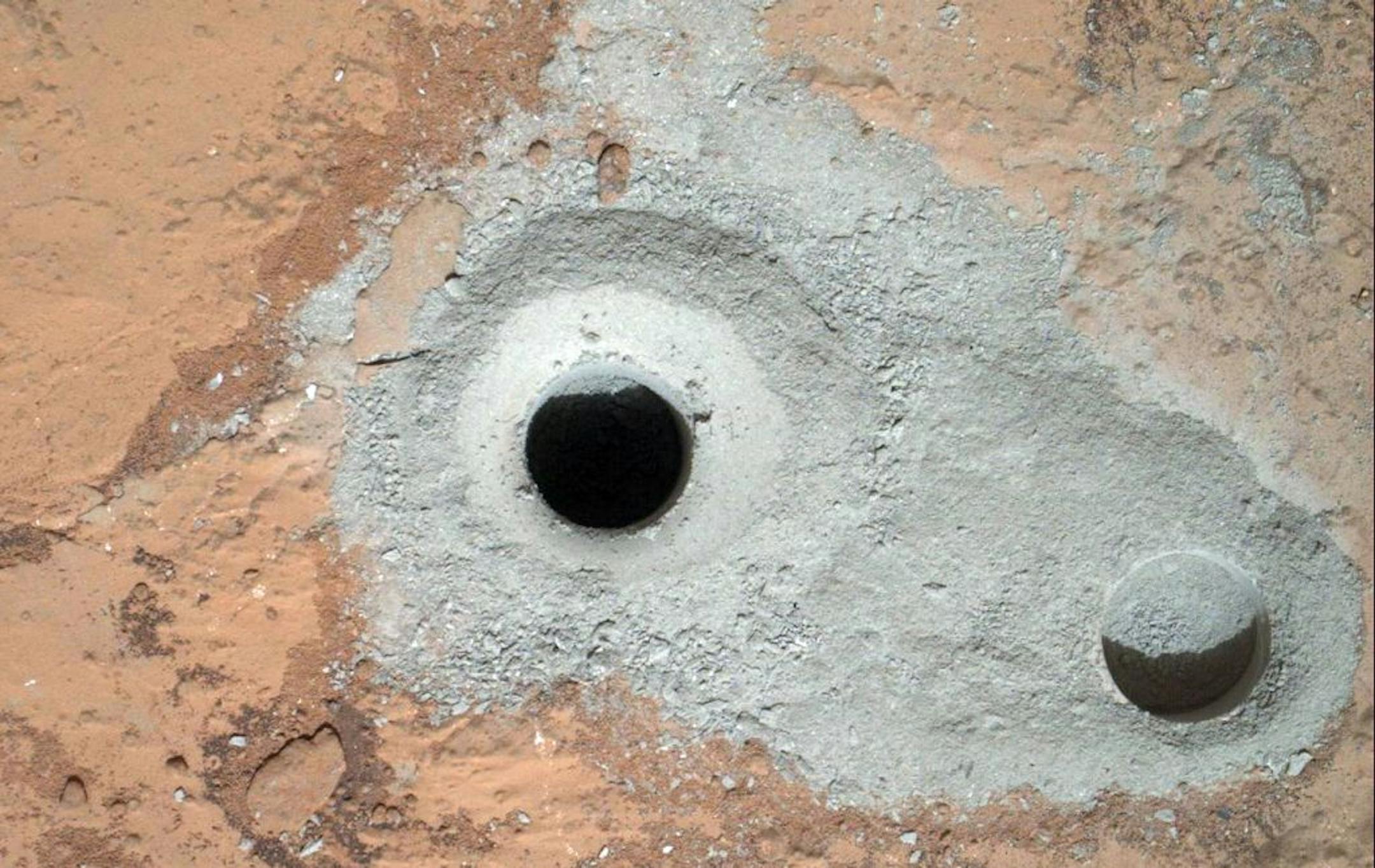 This image released by NASA on Saturday Feb. 9, 2013 shows a fresh drill hole, center, made by the Curiosity rover on Friday, Feb. 8, 2013 next to an earlier test hole. Curiosity has completed its first drill into a Martian rock, a huge milestone since landing in an ancient crater in August 2012.