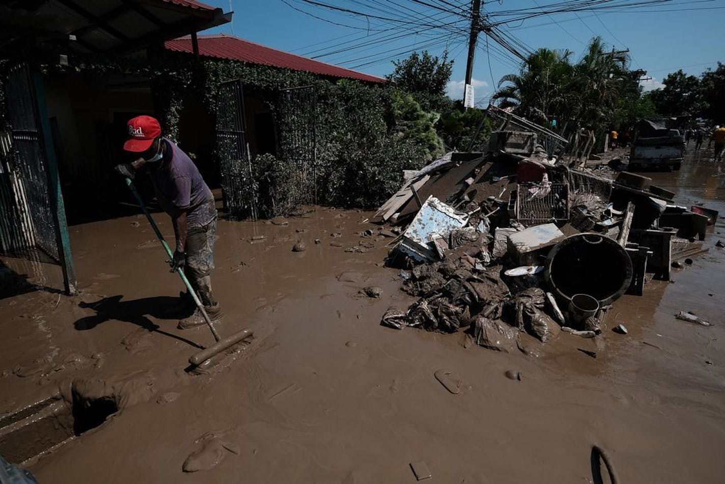 A resident of Colonia Planeta removes mud form the street next to a pile of debris in La Lima, Honduras, after the massive floods produced by Hurricane Eta on November 11, 2020.