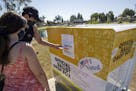 Caitlin Harjes, left, and Angel Santiago, place their ballots inside an official Orange County Registrar of Voters ballot Drop Box for the 2020 Presid