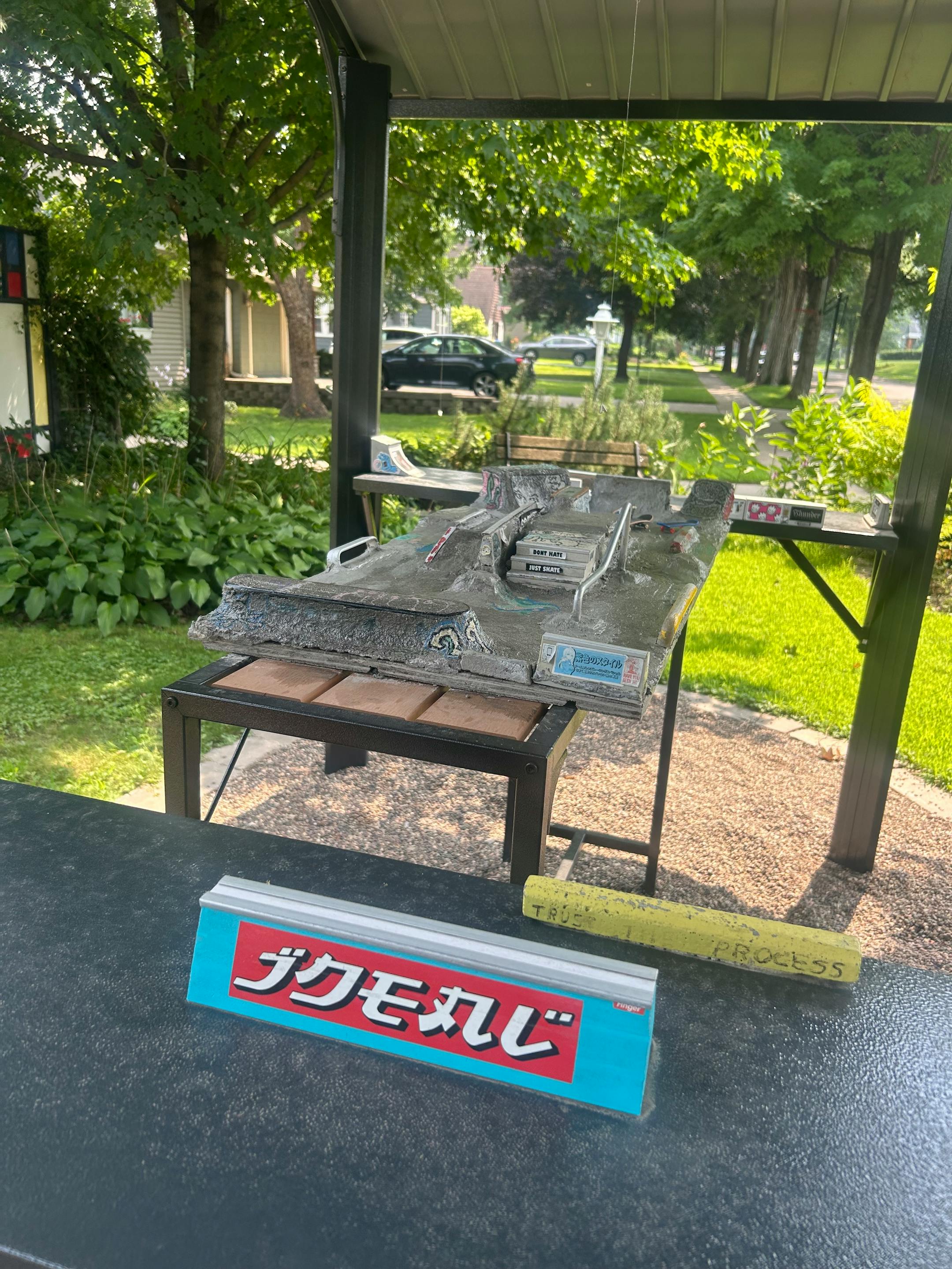 A sheltered table with miniature skate ramps sits in a residential front yard.