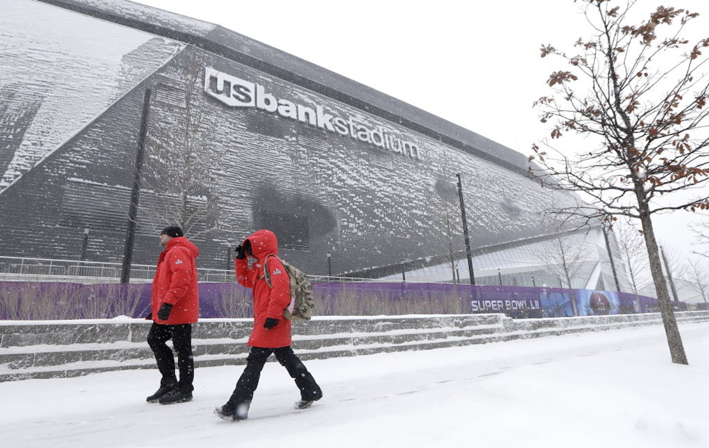 People walk in the snow past U.S. Bank Stadium Saturday, Feb. 3, 2018, in Minneapolis. The New England Patriots and the Philadelphia Eagles are scheduled to play the NFL Super Bowl 52 football game in the stadium Sunday. (AP Photo/Mark Humphrey)