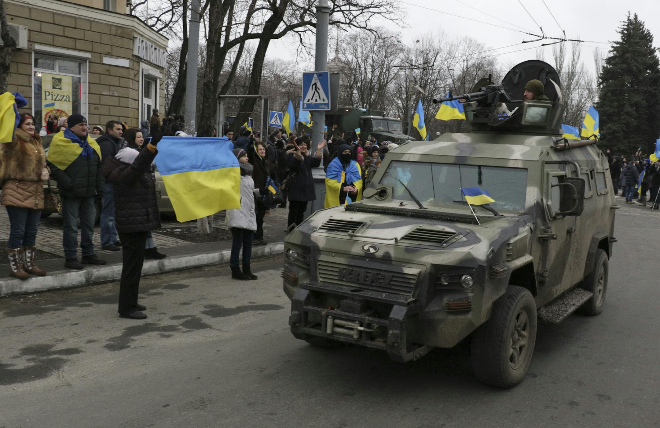 Residents wave Ukrainian flags as they cheer Ukrainian troops coming back to their headquarters after combat operations against Russia-backed separatists in Mariupol, Donetsk region, Ukraine, Wednesday, Feb. 11, 2015.