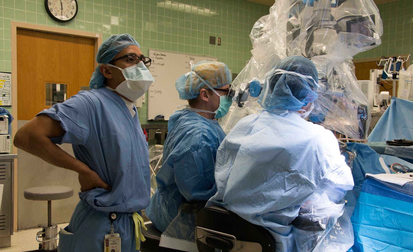 1442: Long procedures requiring tiny, precise movements take a toll on neurosurgeons. Dr. Ciro Vasquez, in his sixth year of training, takes a quick stretch and watches a monitor as his colleagues worked to remove a rare type of brain aneurysm. It took nearly seven hours for assistant professor Dr. Andrew Grande, center, and Dr. Dino Terzic, in his last year of training, to successfully clamp the weakened artery deep inside the patient&#x201a;&#xc4;&#xf4;s left temporal lobe. Photo: Dan Browning